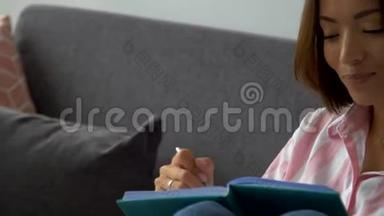 美丽的白人女孩手里拿着一本书坐在沙发上美丽迷人的白人女孩坐在沙发上拿着一个记事本